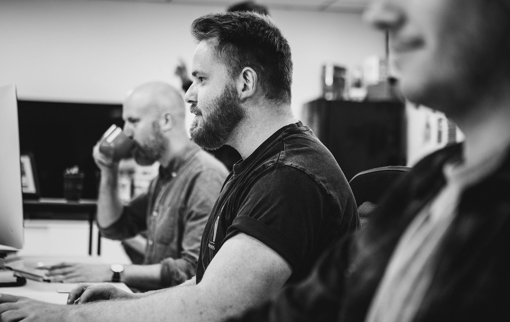 A black and white photograph of Framework’s creative director working on a computer next to two other people.